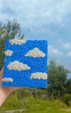 a hand holding up a small piece of blue and white crocheted paper with clouds on it