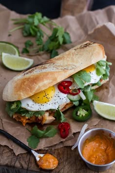 a sandwich with an egg on top and some sauces next to it, sitting on a piece of brown paper