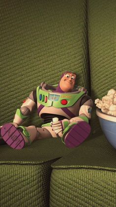 a toy story character sitting on a green couch with a bowl of popcorn in front of him