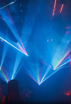 people are standing in front of bright lights at a concert or club, with their hands up to the ceiling