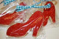 two red shoe shaped cookies wrapped in plastic on a white counter top with a blue ribbon