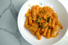 a white bowl filled with pasta on top of a marble counter next to a knife and fork