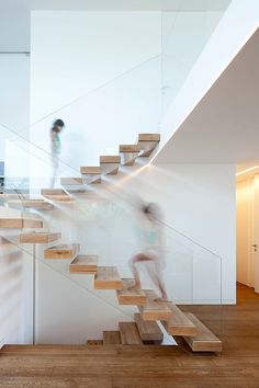 two people walking up and down the stairs in a house with white walls, wood floors and wooden staircases