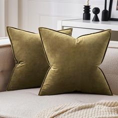 two green velvet pillows sitting on top of a couch next to a white table and lamp