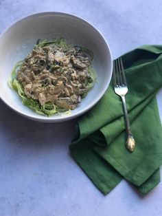 a white bowl filled with pasta and meat on top of a green napkin next to a fork