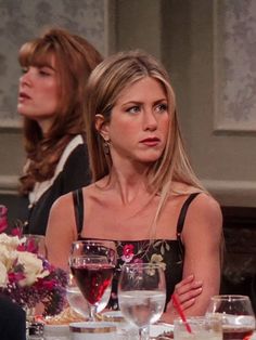 two women sitting at a dinner table with wine glasses on the table and flowers in vases