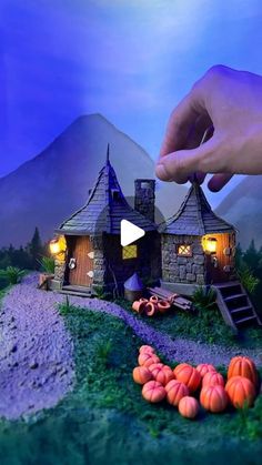 a hand is reaching for a tiny house on a hill with pumpkins in the foreground