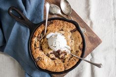 a chocolate chip cookie in a cast iron skillet with ice cream and spoons