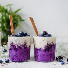 two glasses filled with blueberries and yogurt on top of a white table