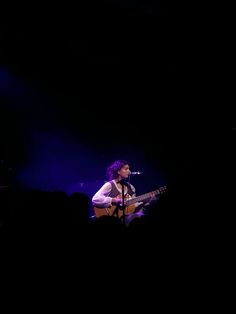 a man that is sitting down with a guitar in his hand and singing into a microphone