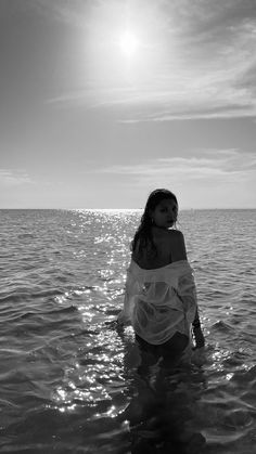 a woman is standing in the water with her arms around her body and looking off into the distance