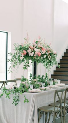 a table with flowers and greenery on it in front of a staircase leading up to the second floor