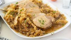 a white plate topped with meat and gravy next to silverware on a table