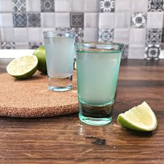 two glasses filled with water sitting on top of a wooden table next to limes