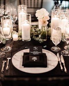 a black and white dinner table setting with candles, napkins, silverware and flowers