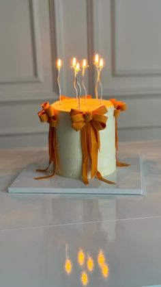 a white cake with orange ribbon and lit candles