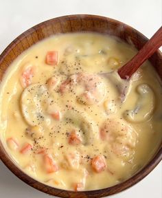 a wooden bowl filled with soup on top of a white table next to a spoon