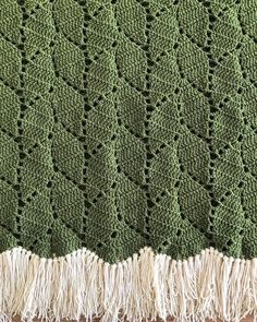 a green crocheted blanket with fringes on it