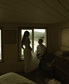 a man and woman standing in front of a window looking out at the water from their bedroom