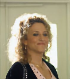 a woman with curly hair is smiling and looking at the camera while standing in front of a door