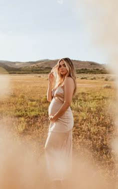 a pregnant woman standing in a field with her hands on her head and looking off to the side