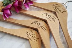 four wooden wedding hangers with names and date engraved on them next to purple flowers