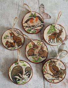 four ceramic ornaments with animals on them hanging from twine strings in front of a white wooden background