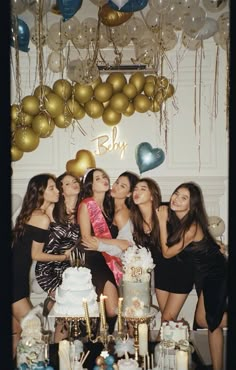 a group of young women standing next to each other in front of a cake and balloons