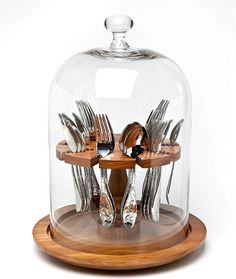 a glass clochet with silverware in it on a wooden plate and holder