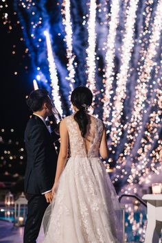 the bride and groom are looking at fireworks in the sky behind them on their wedding day