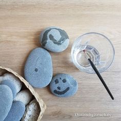 some rocks with faces painted on them next to a glass of water and a straw