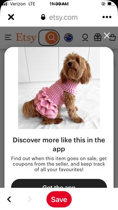 a small dog wearing a pink sweater on top of a white bed next to an iphone