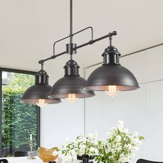 three lights hanging over a dining table in a room with white walls and black chairs