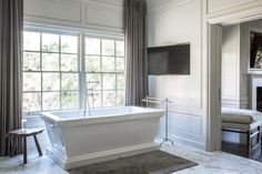 a large white bath tub sitting in a bathroom next to a tv mounted on the wall