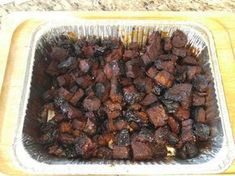 a pan filled with meat sitting on top of a wooden cutting board next to a knife