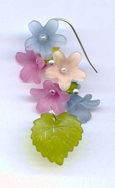 four different colored flowers are hanging from a hook on a white surface with silver earwires