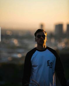 a man standing in front of a cityscape with the sun setting behind him