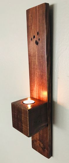 a wooden candle holder with a lit candle on it's side, mounted to the wall