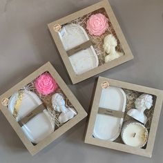 three boxes with different items in them on a table, one is white and the other is pink