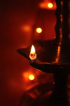 a lit candle sitting on top of a metal plate with lights in the back ground