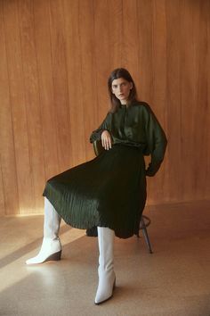 a woman is sitting on a chair wearing white boots and a green pleated dress