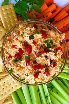 a bowl of tuna salad surrounded by carrots, celery and crackers