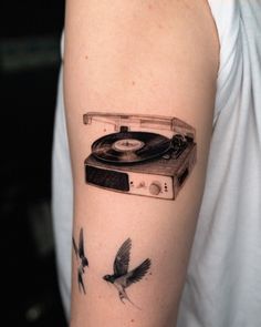 a person with a tattoo on their arm has a record player and two birds flying around