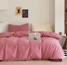 a laptop computer sitting on top of a bed covered in pink and white striped sheets