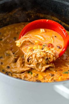 a ladle full of chicken tortilla soup being stirred with a red spoon