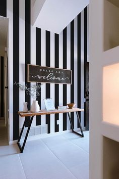 a black and white striped wall with a wooden table in the foreground that says welcome