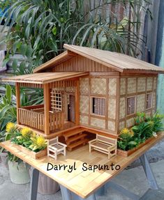 a doll house sitting on top of a wooden table next to potted plants and trees