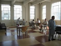 several people sitting at tables in a large room with checkered flooring and windows