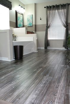 a bathroom with wood flooring and gray curtains on the window sill next to the tub