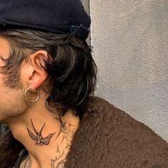 a man with a bird tattoo on his neck wearing a brown sweater and gold hoop earrings